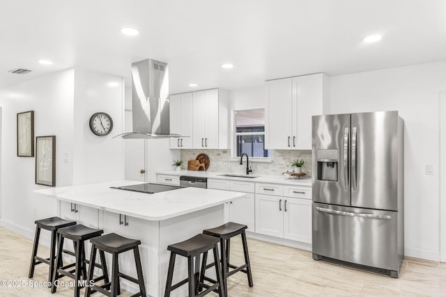 kitchen featuring baseboards, a kitchen breakfast bar, wall chimney exhaust hood, a sink, and appliances with stainless steel finishes