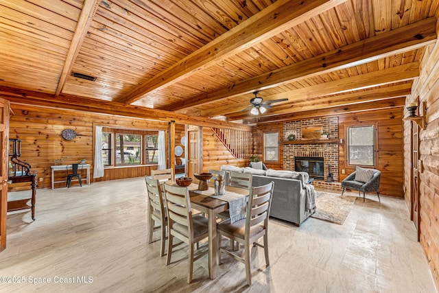 dining area with ceiling fan, a brick fireplace, wooden ceiling, light wood-type flooring, and beamed ceiling