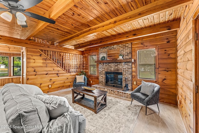 living room featuring a ceiling fan, a brick fireplace, wood walls, wooden ceiling, and beamed ceiling