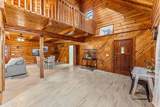 foyer with a towering ceiling, beamed ceiling, ceiling fan, wooden walls, and wooden ceiling