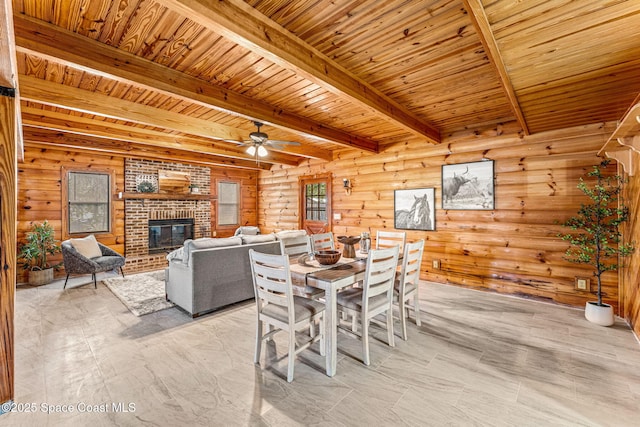 dining room featuring ceiling fan, beam ceiling, a brick fireplace, wooden ceiling, and rustic walls