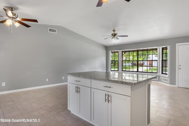 kitchen with light stone counters, a center island, a ceiling fan, vaulted ceiling, and visible vents