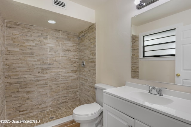 bathroom featuring toilet, visible vents, tiled shower, and vanity