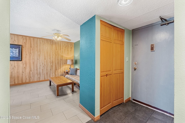 foyer entrance featuring baseboards, wood walls, a ceiling fan, a textured ceiling, and tile patterned floors