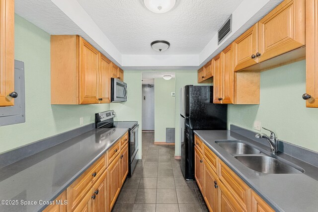 kitchen featuring stainless steel appliances, a sink, a textured ceiling, dark countertops, and dark tile patterned floors