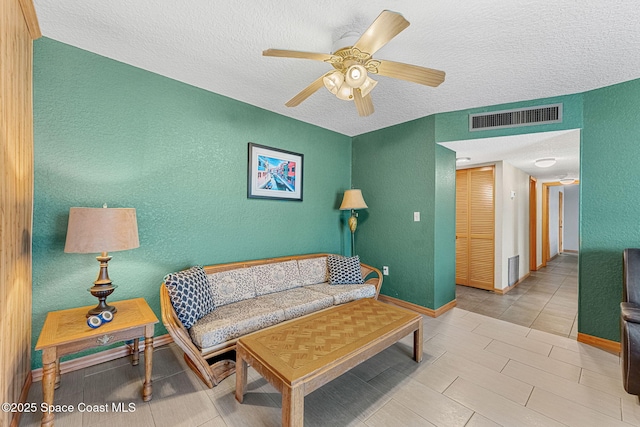 living area with a textured wall, a textured ceiling, ceiling fan, and baseboards
