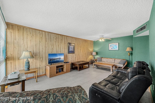 living area with wooden walls, ceiling fan, and a textured ceiling