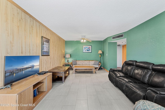 living room featuring a textured ceiling, ceiling fan, and wooden walls