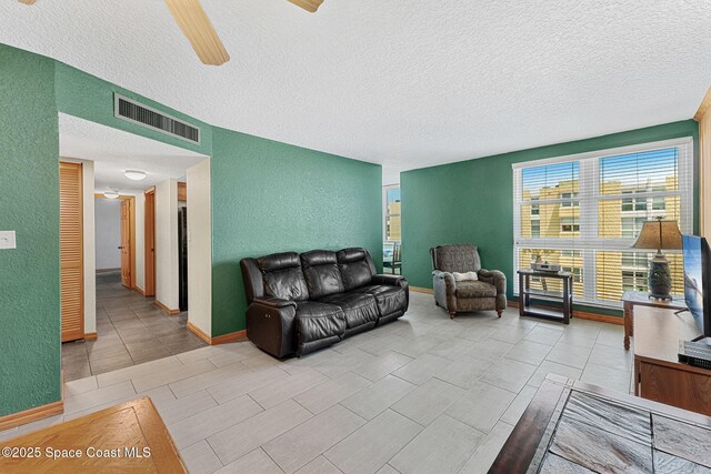 living room featuring a textured wall, a textured ceiling, ceiling fan, and baseboards