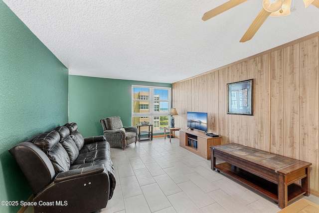 living room featuring wood walls, a textured ceiling, ceiling fan, and a textured wall