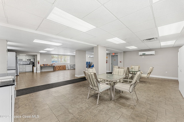 dining area featuring a wall mounted air conditioner, light tile patterned flooring, a drop ceiling, and baseboards