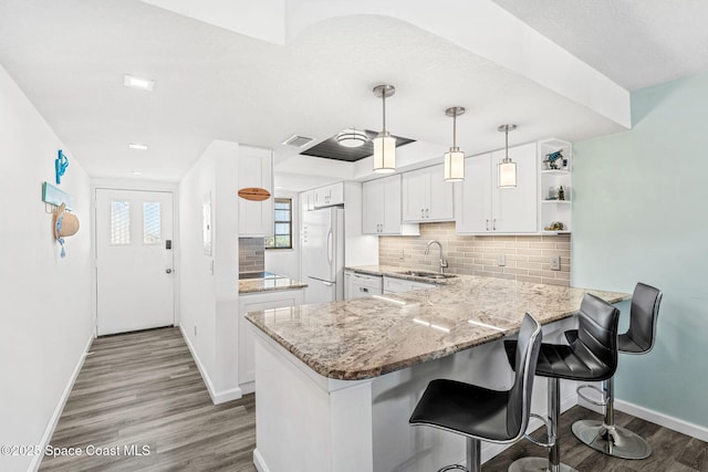 kitchen featuring freestanding refrigerator, wood finished floors, baseboards, a sink, and backsplash