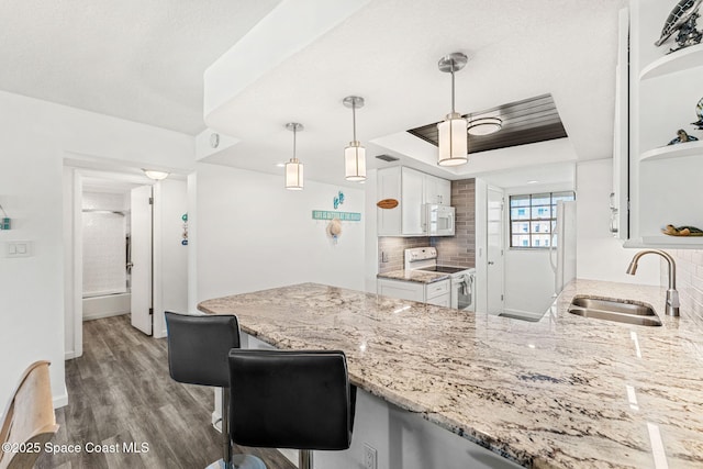 kitchen with a peninsula, white appliances, white cabinetry, a sink, and backsplash