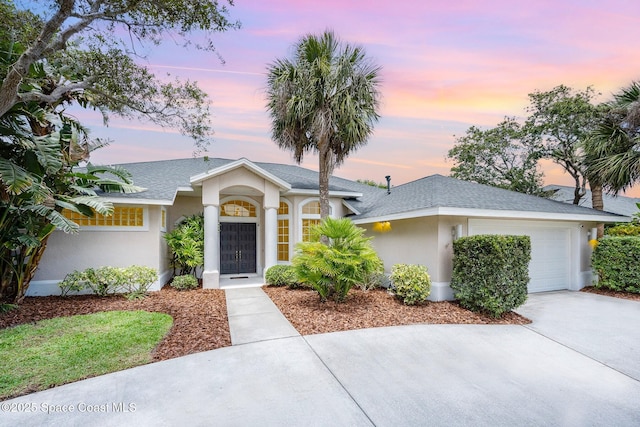 view of front of property with a garage, stucco siding, a shingled roof, and concrete driveway