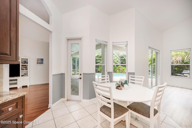 dining area with light wood-style floors, baseboards, a healthy amount of sunlight, and high vaulted ceiling