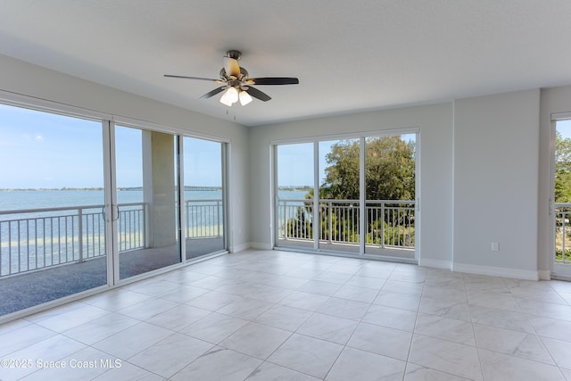 unfurnished room with a water view, a ceiling fan, plenty of natural light, and baseboards