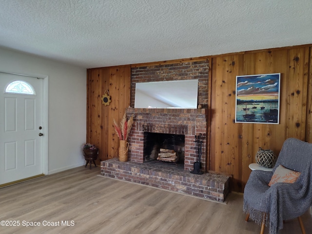 living area with wood walls, wood finished floors, a fireplace, baseboards, and a textured ceiling