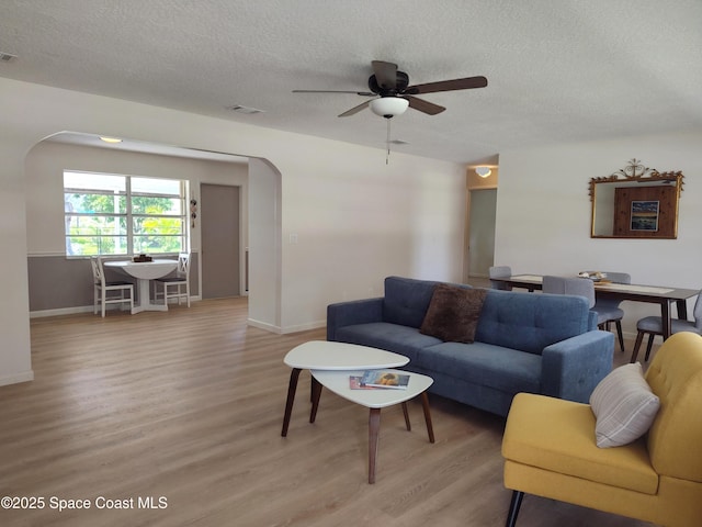 living room with light wood-style floors, arched walkways, a textured ceiling, and ceiling fan