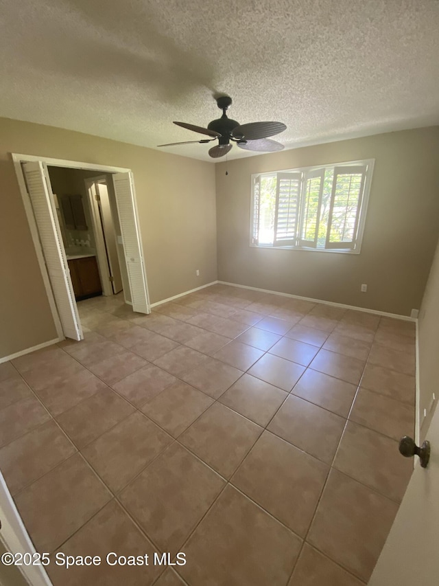 unfurnished bedroom featuring a textured ceiling, light tile patterned floors, baseboards, and ceiling fan