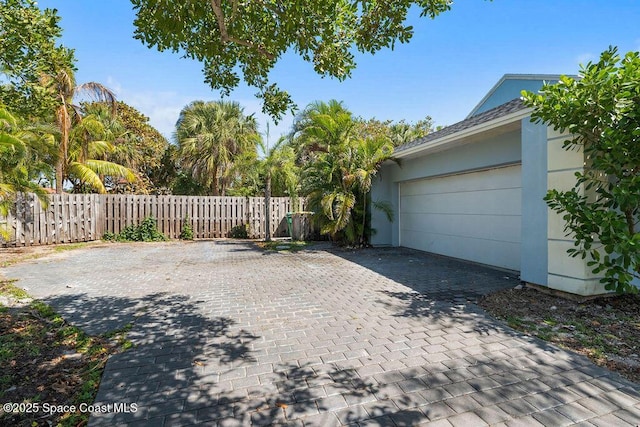 exterior space with fence, an attached garage, and decorative driveway