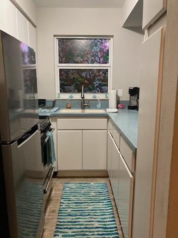 kitchen with a sink, light wood finished floors, light countertops, stainless steel appliances, and white cabinetry