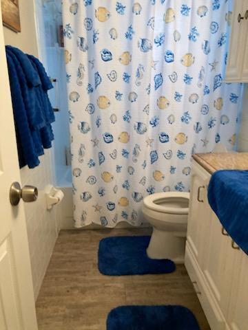 bathroom with toilet, wood finished floors, and shower / bath combo with shower curtain
