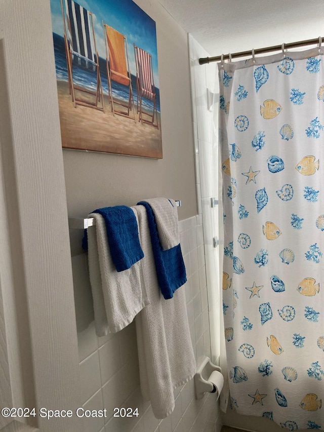 full bathroom with a wainscoted wall, curtained shower, and tile walls