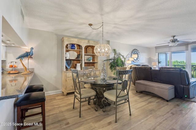 dining space with light wood-type flooring, a ceiling fan, a chandelier, baseboards, and a textured ceiling