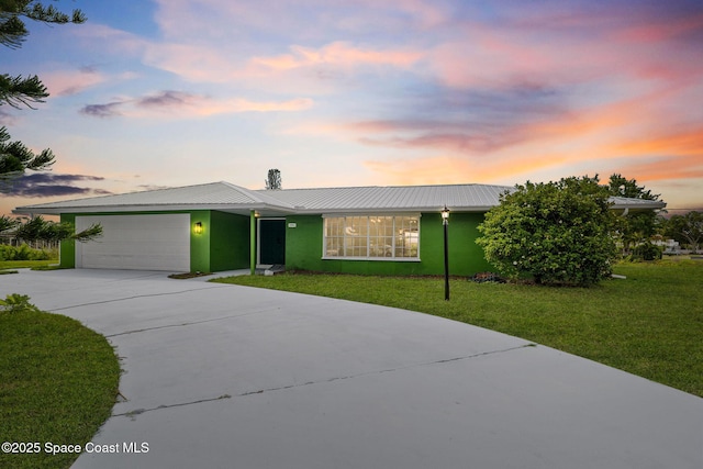 view of front facade featuring concrete driveway, an attached garage, a front yard, metal roof, and stucco siding