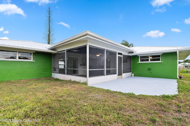 back of house with a sunroom, a lawn, a patio, metal roof, and stucco siding