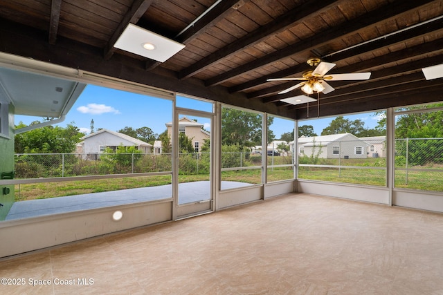 unfurnished sunroom with beam ceiling, a ceiling fan, and a residential view