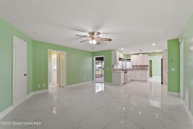 unfurnished living room featuring ceiling fan, baseboards, light marble finish flooring, a sink, and a textured ceiling