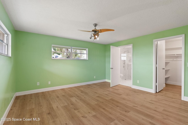 unfurnished bedroom featuring a walk in closet, light wood-style floors, baseboards, a textured ceiling, and ensuite bathroom