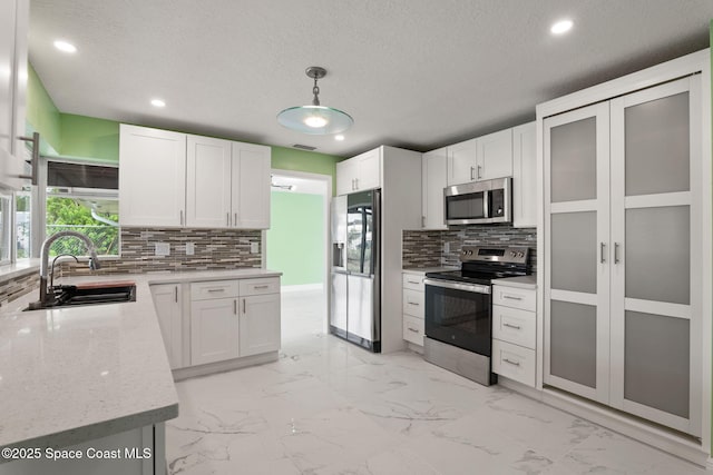 kitchen featuring appliances with stainless steel finishes, a sink, tasteful backsplash, healthy amount of natural light, and a textured ceiling