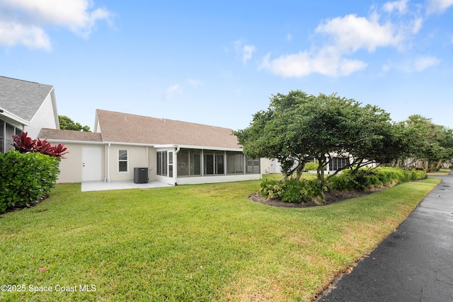 rear view of house featuring stucco siding, a sunroom, central AC unit, a patio, and a yard