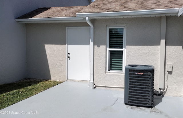 property entrance with central AC, a shingled roof, and stucco siding