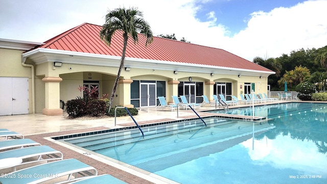 back of house with a community pool, stucco siding, a standing seam roof, a patio area, and metal roof