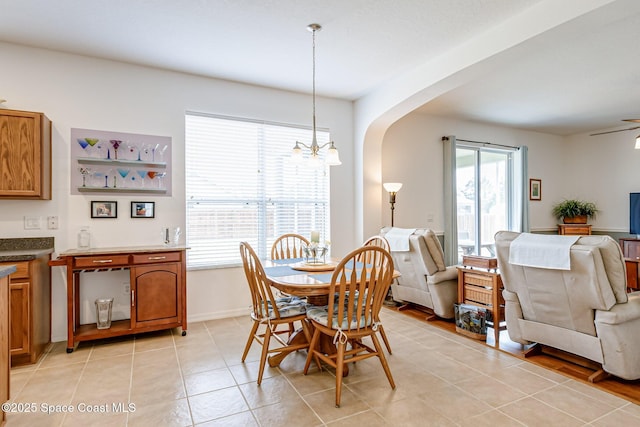 dining space featuring arched walkways, baseboards, light tile patterned floors, and ceiling fan with notable chandelier