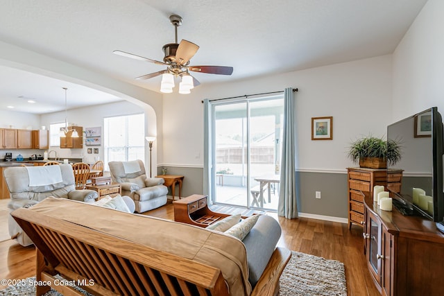 living room with baseboards, wood finished floors, a ceiling fan, and arched walkways