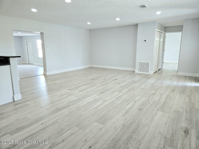 unfurnished living room featuring a textured ceiling, visible vents, and light wood-type flooring