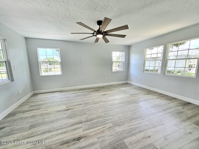spare room featuring baseboards, ceiling fan, light wood-type flooring, and a textured ceiling