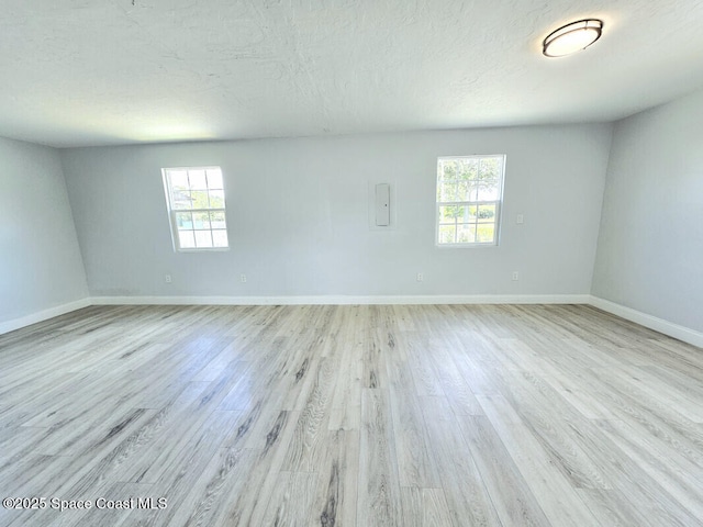 empty room with a textured ceiling, baseboards, plenty of natural light, and light wood-style flooring