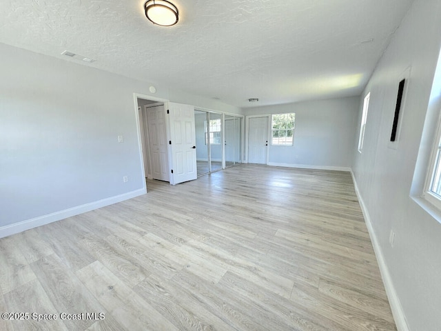 unfurnished room featuring a textured ceiling, baseboards, visible vents, and light wood-style floors