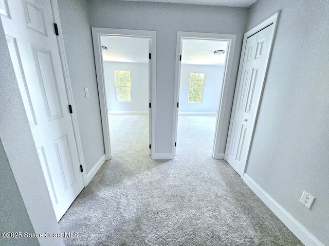 corridor featuring baseboards and light colored carpet