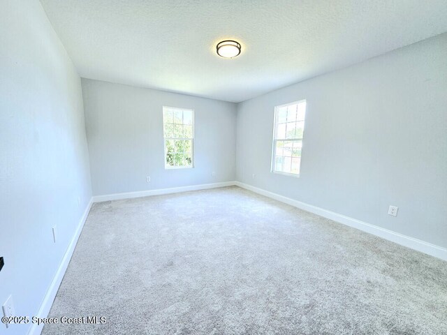 carpeted empty room featuring a textured ceiling, baseboards, and a wealth of natural light