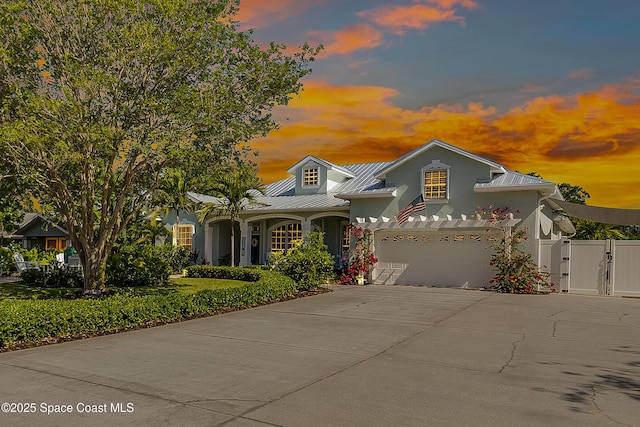 traditional-style house featuring driveway, stucco siding, metal roof, and a gate