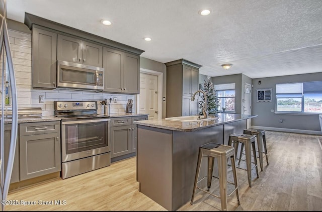 kitchen featuring a sink, stainless steel appliances, a kitchen island with sink, light wood-type flooring, and stone counters