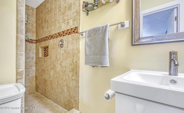 full bathroom with toilet, a tile shower, a sink, and a textured wall