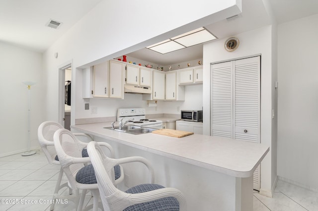kitchen with under cabinet range hood, white range with electric stovetop, visible vents, stainless steel microwave, and a peninsula