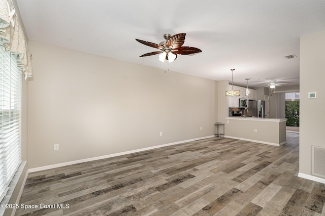 unfurnished living room with a ceiling fan, baseboards, visible vents, and wood finished floors